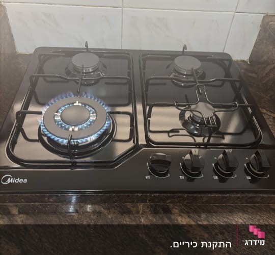 כיריים גז שחורות מותקנות על משטח שיש במטבח עם להבה דולקת